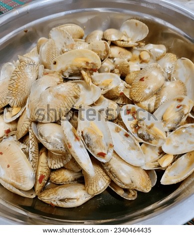 a photography of a bowl of clams with a spoon in it, there is a bowl of clams in a bowl on a table.