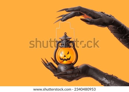 Black hands of witch with lantern on orange background. Halloween celebration