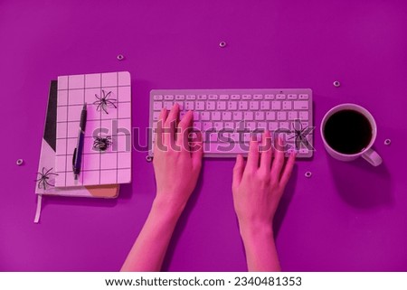 Female hands with modern computer keyboard, cup of coffee, notebooks and spiders for Halloween on purple background