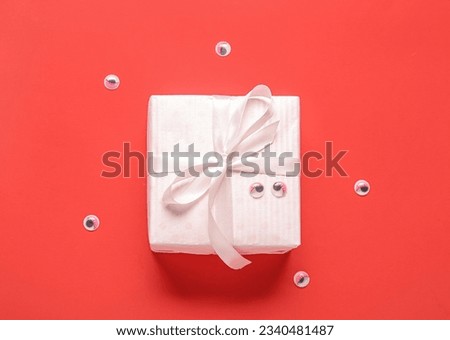 Composition with beautiful gift box and eyes for Halloween on red background, closeup
