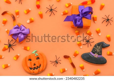 Frame made spiders, gift boxes, tasty candy corns and cookies for Halloween on orange background