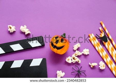 Tasty popcorn, clapperboard, pumpkin and straws on purple background, closeup. Halloween celebration