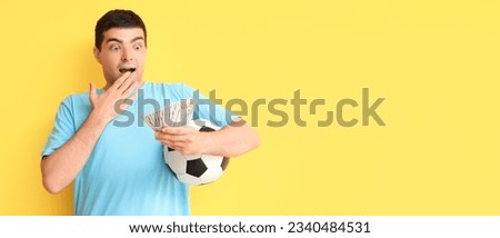Surprised young man with soccer ball and money on yellow background with space for text. Sports bet concept