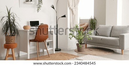 Interior of light living room with grey sofa, modern workplace and houseplants Royalty-Free Stock Photo #2340484545