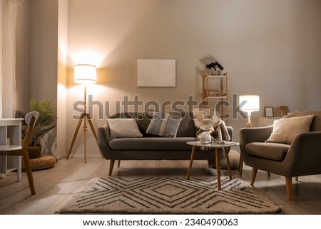 Interior of living room with cozy grey sofa, armchair and glowing lamps Royalty-Free Stock Photo #2340490063