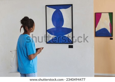 Minimal back view of black teen girl looking at abstract art in art gallery or museum, copy space Royalty-Free Stock Photo #2340494477