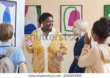 Waist up portrait of smiling black woman with group of teenagers in art gallery or museum