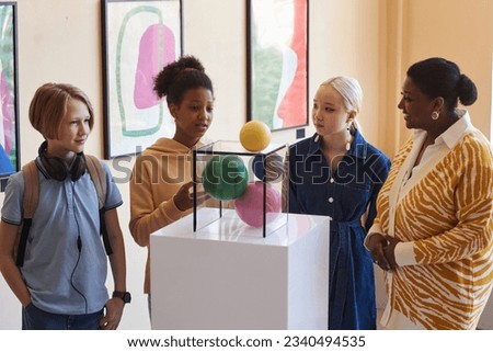 Diverse group of school children listening to teacher or tour guide while looking at sculptures Royalty-Free Stock Photo #2340494535