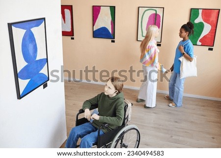 High angle portrait of teenage boy with disability looking at abstract pictures in art gallery and listening to audio guide, copy space