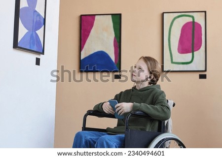 Side view portrait of teenage boy with disability looking at pictures in art gallery and listening to audio guide, copy space
