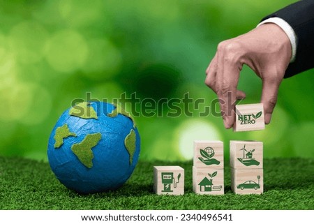 Businessman hand with paper globe and net zero symbol cube for eco awareness. Ethical company reduce CO2 emission, fight climate change and global warming by clean energy for green environment. Alter