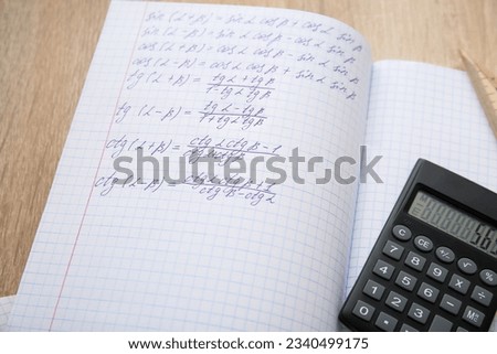 Open copybooks with math formulas and calculator on wooden table, closeup