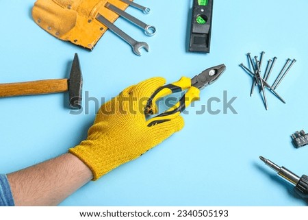 Male hand in gloves holding pliers near different instruments on blue background Royalty-Free Stock Photo #2340505193