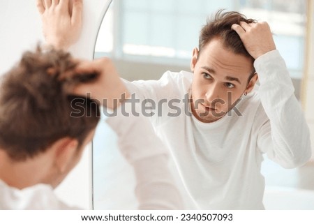 Young man with hair loss problem looking in mirror at home Royalty-Free Stock Photo #2340507093