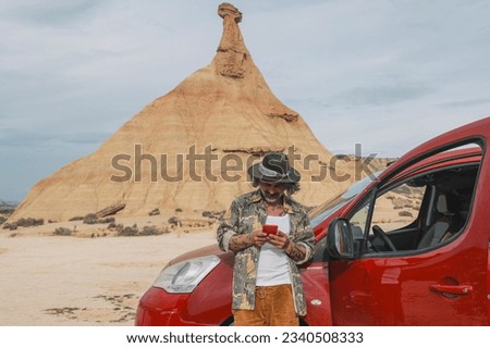 Middle aged traveler looking at cell phone in desert landscape of Bardenas Reales, Arguedas, Navarra, Spain