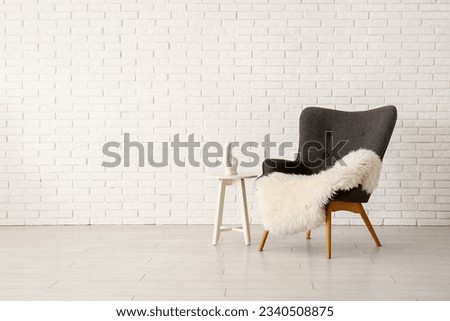 Stylish black armchair, blanket and chair near brick wall