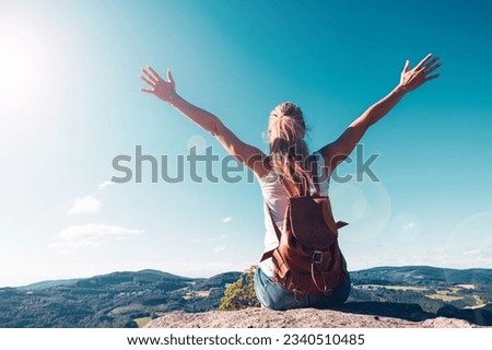 Woman sitting on a peak with backpack and arms raised against blue sky- freedom, achievement,travel,adventure concept Royalty-Free Stock Photo #2340510485