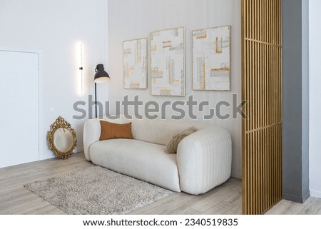 a soft comfortable sofa with a floor lamp is an open-plan apartment in a modern style with light walls and wooden floors and a stylish golden partition Royalty-Free Stock Photo #2340519835