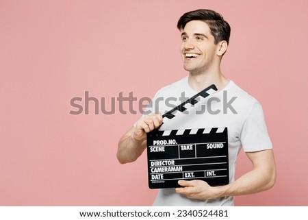 Young caucasian man wear white t-shirt casual clothes hold in hand classic black film making clapperboard look aside isolated on plain pastel light pink background studio portrait. Lifestyle concept