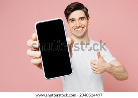 Young man wear white t-shirt casual clothes hold in hand using close up mobile cell phone in blue case with blank screen workspace area show thumb up isolated on plain pastel pink background studio Royalty-Free Stock Photo #2340524497