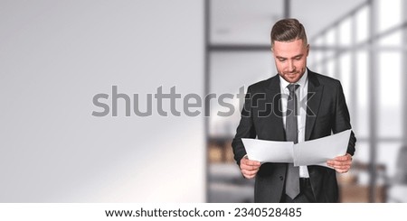 Businessman reading business documents in hands. Concentrated man portrait in black formal suit, studying financial report. Copy space empty white office wall. Concept of contract Royalty-Free Stock Photo #2340528485