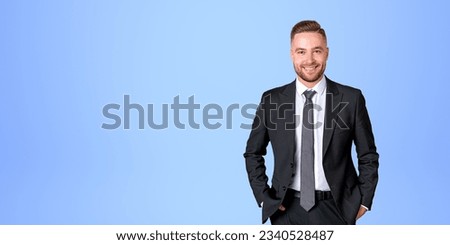 Successful businessman in black formal suit, hands in pocket and happy looking at the camera on empty copy space blue background. Concept of business start up and investment Royalty-Free Stock Photo #2340528487