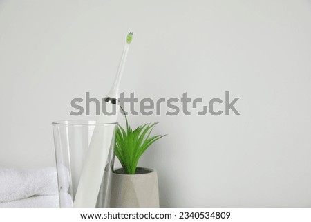 Electric toothbrush in glass and green houseplant on light background. Space for text