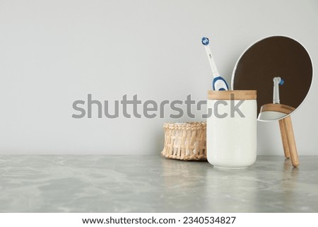 Electric toothbrush in holder, mirror and towel on light grey marble table near white wall. Space for text