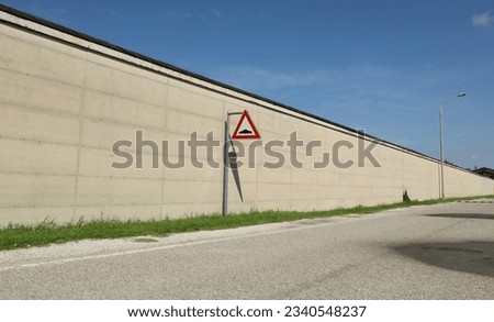 Speed bump ahead, road sign, next to a long concrete wall. Strip of grass and road in front. Background for copy space.