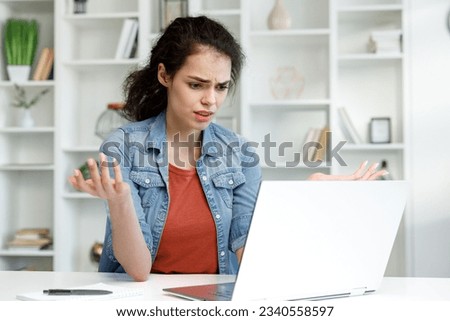 Disappointed girl looks at the laptop screen, does not understand what happened. Brunette woman is angry that the computer broke. Royalty-Free Stock Photo #2340558597