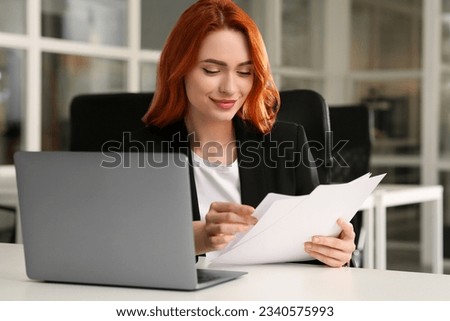 Woman with papers working near laptop at white desk in office