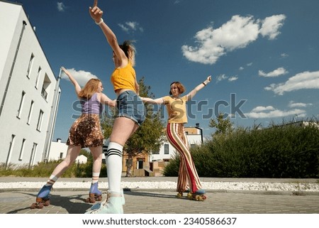 Three happy girls whirling on roller skates in front of camera and having fun while enjoying leisure on summer day in urban environment Royalty-Free Stock Photo #2340586637