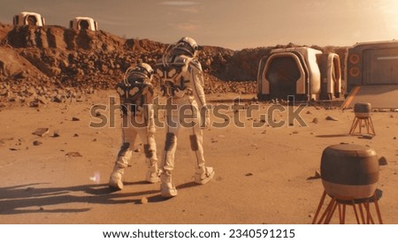 Two astronauts in spacesuits walk toward research station, colony or scientific base on Mars. AI powered rover rides in the background. Space mission. Futuristic colonization and exploration concept. Royalty-Free Stock Photo #2340591215