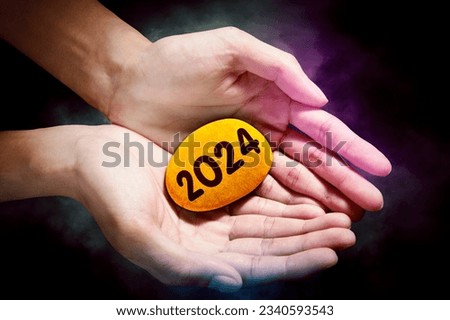 Concept of New Year 2024. Picture of hand holding a stone pebble with the 2024 new year numbers