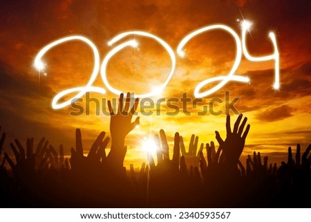Silhouette of crowd hands celebrating the 2024 new year outdoors at sunset or sunrise