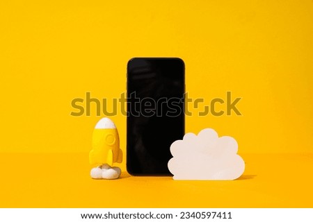 Black smartphone with paper cloud and rocket on yellow background, cloud computing concept