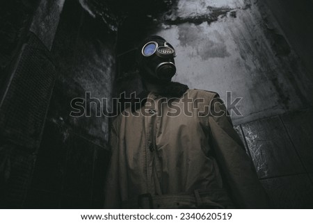 A man wearing a gas mask inside a ruined building with a leaky roof in the dark, apocalypse, good for book cover, low angle Royalty-Free Stock Photo #2340620519