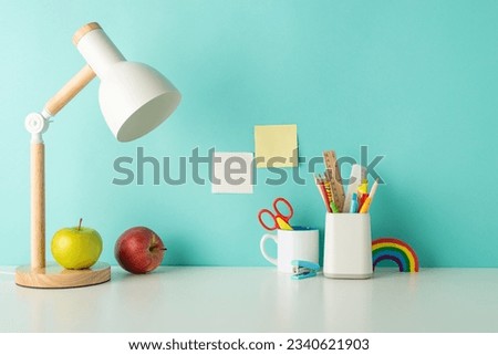 Empower students with an organized study zone through this side-view picture featuring white desk with lively school supplies in penholder and lamp on a blue backdrop, suitable for text or ad usage Royalty-Free Stock Photo #2340621903