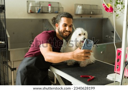 Excited man working as a pet groomer taking a picture with a beautiful maltese dog after a haircut and a bath at the spa