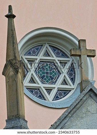 Religion symboles on a church in village Vidče near to Rožnov pod Radhoštěm in Czech republic. Concrete cross and six-pointed star aka hexagram on glass mosaic window.