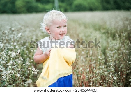 Proud Ukrainian little girl stands on field of mature buckwheat in a yellow-blue flag. day of Ukraine's insability. Selective focus on flag