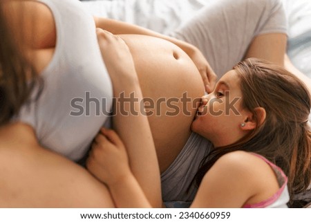 Picture of future big sister kissing mom's belly while lying on her lap, mom holding her hands on and under her belly
