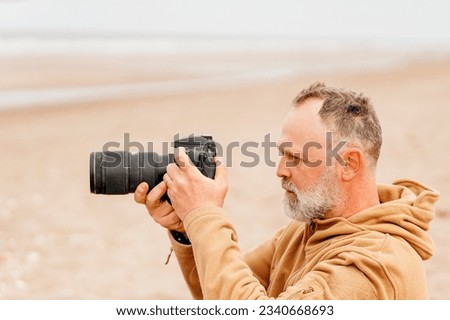 portrait of a bearded man photographing the sea on the beach in autumn