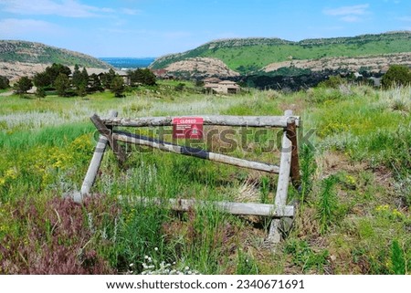 Buck fence with Closed Trail sign along hiking trail in mountains, green grass with wildflowers meadow natural landscape. Restricted access due to habitat restoration. Barrier, obstacle concept.