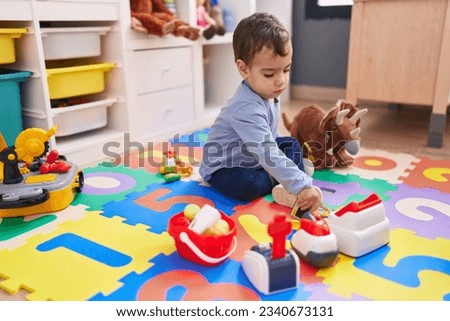 Adorable hispanic boy playing supermarket game sitting on floor at kindergarten