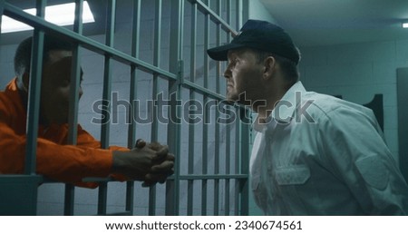 Warden brings guilty prisoner in jail cell and takes off handcuffs. African American man serves imprisonment term in correctional facility or detention center. Murderer in prison cell. Royalty-Free Stock Photo #2340674561