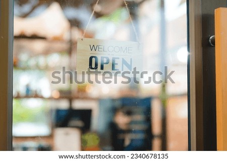 Hand of coffee shop staff woman wearing apron turning open sign board on glass door in modern cafe, morning of hotel service or restaurant retail store, small business owner in food and drink concept