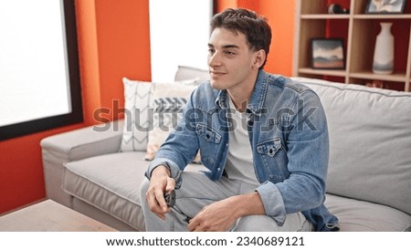 Young hispanic man watching tv sitting on sofa at home