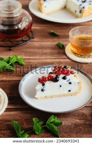 Dessert, sliced round cheesecake with blackcurrant on shortcrust pastry on a ceramic plate on a wooden background. Summer desserts, pastries with berries. Recipes dairy products. American cuisine.