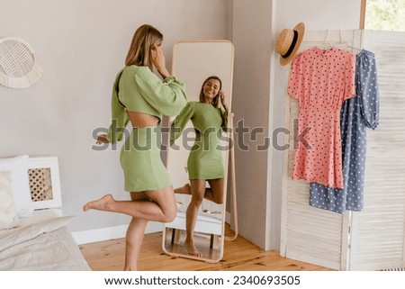 young pretty woman in green dress trying on fashion style trend dress looking in mirror at home or showroom Royalty-Free Stock Photo #2340693505